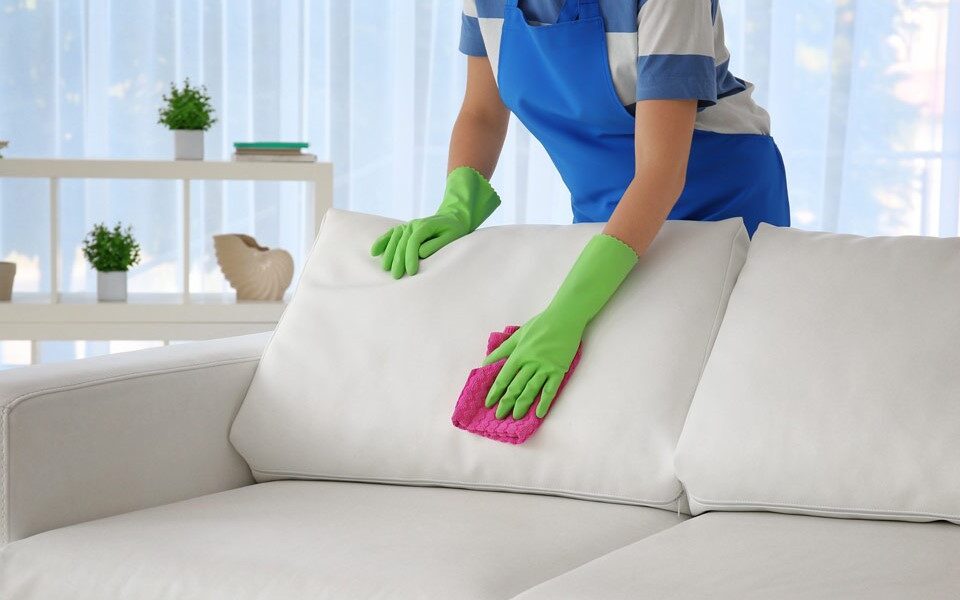 A woman in blue and white cleaning a couch. Professional sofa cleaning service in Dubai.