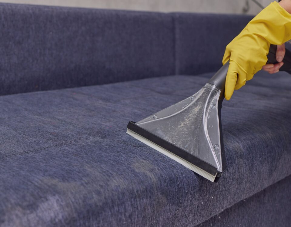 A person using a vacuum to clean a blue couch in Dubai.